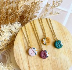 three necklaces with different designs on them sitting on a wooden plate next to dried plants