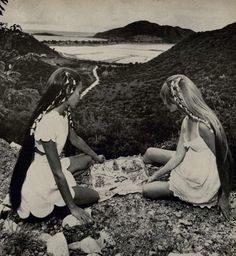 two women sitting on top of a hill next to each other