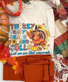 a white shirt with an image of a turkey on it next to fall leaves and pumpkins