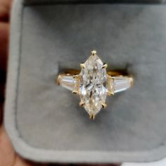 an engagement ring with three stones in the middle and two diamonds on each side, sitting inside a box