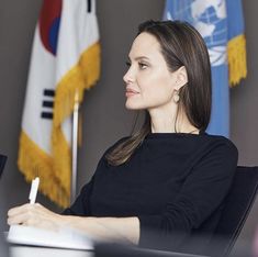 a woman sitting at a desk with a pen in her hand and two flags behind her