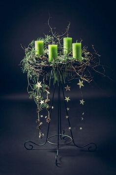 four green candles sitting on top of a metal stand with greenery and stars around it