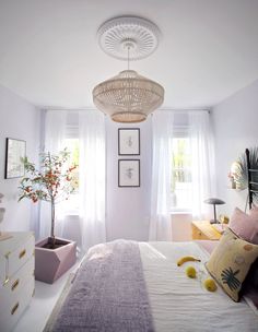 a bed room with a neatly made bed and a lamp hanging from the ceiling next to a window