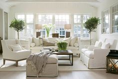 a living room filled with white furniture and lots of windows in it's walls