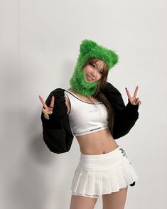 a woman in a green furry hat and skirt posing for the camera with her peace sign