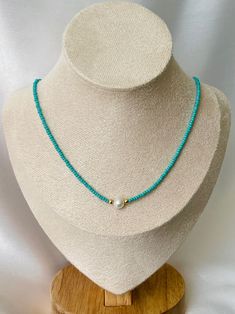 Uniquely crafted, this turquoise seed bead necklace features a single lustrous pearl as its centerpiece, radiating elegance and charm. Hand-threaded with precision, the delicate turquoise seed beads create a shimmering backdrop, accentuating the timeless beauty of the solitary pearl. Designed to withstand water, this necklace is as resilient as it is captivating. Available in lengths of 14 to 18 inches, it serves as a sophisticated accessory, effortlessly adding a touch of refinement to any outf Turquoise Beaded Necklace With Pearl Charm As Gift, Adjustable Turquoise Pearl Necklace With Round Beads, Handmade Turquoise Pearl Beaded Necklaces, Handmade Turquoise Pearl Beaded Necklace, Handmade Turquoise Pearl Necklace With Round Beads, Turquoise Beach Necklace With Round Spacer Beads, Turquoise Pearl Necklace With Pearl Charm As Gift, Turquoise Pearl Necklace Gift, Turquoise Pearl Jewelry With Round Beads