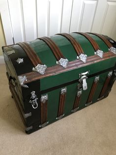 a green and black trunk sitting on top of a carpeted floor next to a white door