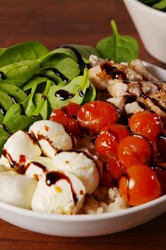 a white bowl filled with vegetables and meat on top of a wooden table next to a green leafy salad