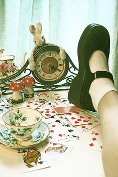 a table topped with lots of tea cups and saucers next to a small clock