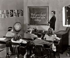 an old black and white photo of children sitting at desks in front of a chalkboard