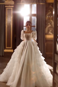 a woman in a wedding dress standing on a wooden floor with her arms behind her back