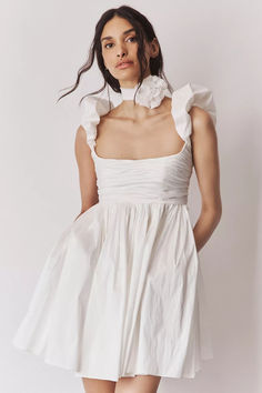 a woman is wearing a white dress with ruffles on the neck and shoulders