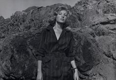 black and white photograph of woman standing in front of rock formation with her hands on her hips