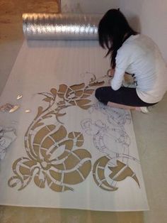 a woman sitting on top of a white floor next to a roll of paper with designs on it