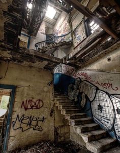 an abandoned building with graffiti all over the walls and staircase leading up to it's second floor