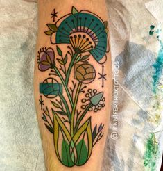 a tattoo on the leg of a person with flowers and leaves in it, sitting on top of a sheet of paper