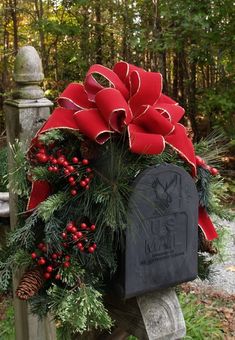 a christmas wreath with red bows and pine cones on the front of a grave surrounded by evergreens