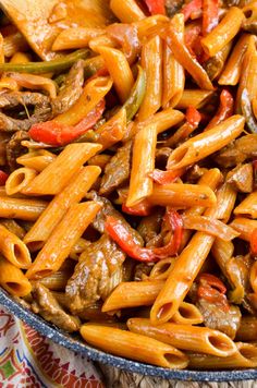 pasta with meat and peppers in a skillet on a colorful cloth next to a wooden spoon