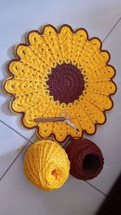 a crocheted sunflower sits on the floor next to yarn and balls of thread