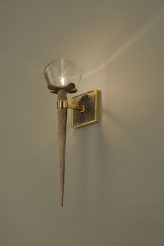 a wall mounted light on the side of a white wall next to a glass vase