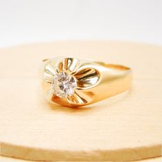 a gold ring with a diamond in the center sitting on a wooden stand, against a white background