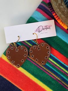 "Looking for lovely Latino-inspired polymer clay earrings? Grab this hand-painted pair of glazed cazuelita style, barro pottery heart earrings. Handmade here in the Alamo City, these Mexican-style earrings are perfect for a Valentine's date or any day you want to represent your love for your culture! These earrings are grand (1.5\") making them a beautiful statement piece. Each set is secured to 25k gold-toned, nickel-free clasp hooks. All earrings are lightweight and made of quality FIMO brand polymer clay, with the fine-detailed designs being hand-painted with acrylic. UV resin is used to lock in protection on the hand painted design. Properly fitted backings are included. Fall in love with this pair? Put it in your cart! Follow me @dovetailcraftique on Instagram, Facebook, TikTok, and P Mexican Style Clay Earrings, Artisan Heart Earrings For Pierced Ears As Gift, Artisan Heart Earrings As Gift, Hand Painted Heart Earrings For Valentine's Day Gift, Heart-shaped Polymer Clay Earrings For Gifts, Polymer Clay Heart Earrings As Gift, Unique Hand Painted Heart Earrings, Hand Painted Dangle Heart Earrings As Gift, Hand Painted Heart Earrings For Gift