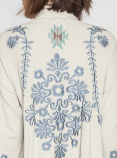 the back of a woman's sweater with blue and white embroidered flowers on it