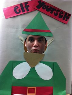 a man wearing a green elf costume standing in front of a white wall