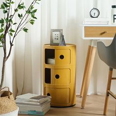 a yellow cabinet sitting next to a tree in a room with white walls and wooden floors