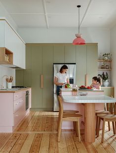 a woman and child are in the kitchen with pink cabinets, white countertops and wood floors