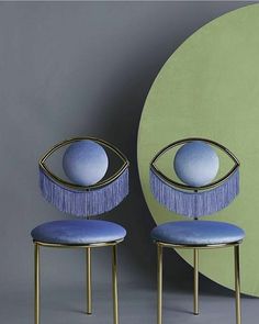 two blue chairs with fringes on them in front of a green wall and circular object