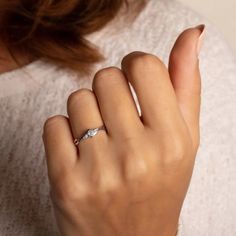 a woman's hand with a diamond ring on her left wrist, wearing a white sweater