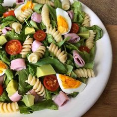 pasta salad with ham, egg and tomatoes on a white plate sitting on a wooden table