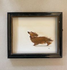 a painting of a brown dog in a black frame on a white wall behind it