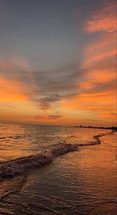 an orange and blue sunset over the ocean with waves coming in from the shore line