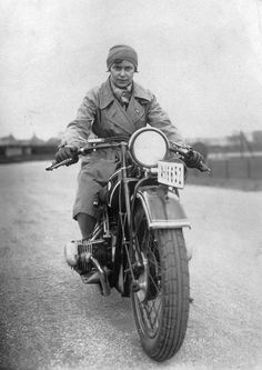 a man riding on the back of a motorcycle down a country road in an old photo