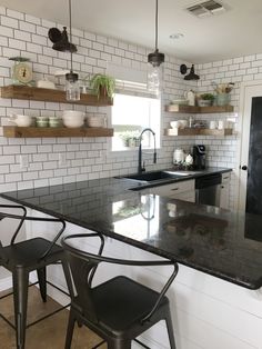 a kitchen with black counter tops and white brick wall behind the bar stools, along with hanging potted plants