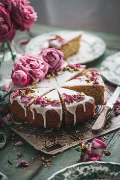 a cake with white icing and pink flowers on it sitting on a table next to plates