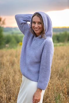 a woman standing in a field wearing a blue sweater and white skirt with her hands on her head