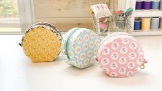 four small round purses sitting on top of a table next to thread spools