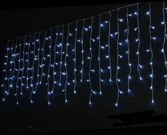 blue lights are hanging from the side of a building at night time, with long strands of white leds strung across the entire wall