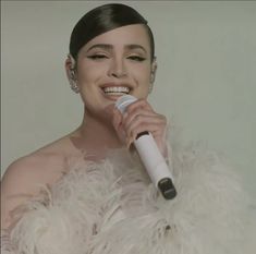 a woman wearing a white feather coat holding a microphone in her right hand and smiling at the camera