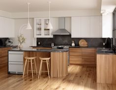 a kitchen with wooden floors and white cabinets, black counter tops and two stools