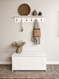 a white bench with two hooks on the wall above it and a potted plant next to it