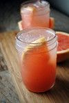 three glasses filled with watermelon and lemonade sit on a cutting board next to sliced grapefruit