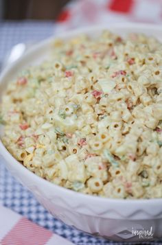 a white bowl filled with macaroni salad on top of a checkered table cloth