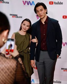 a man and woman standing next to each other in front of a red carpeted wall