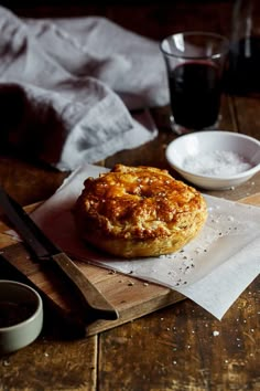 a pastry sitting on top of a wooden cutting board next to a bowl and knife