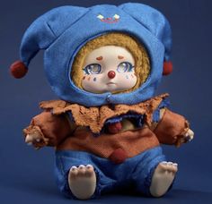 a creepy doll with blue eyes sitting on a blue surface and wearing a clown outfit