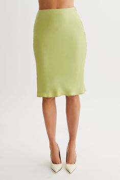 a woman is wearing a green skirt and high heels with her hands on her hips